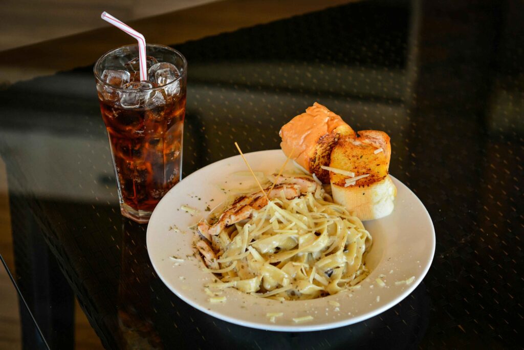 Close-Up Shot of a Plate of Pasta Carbonara beside a Glass of Soft Drink.