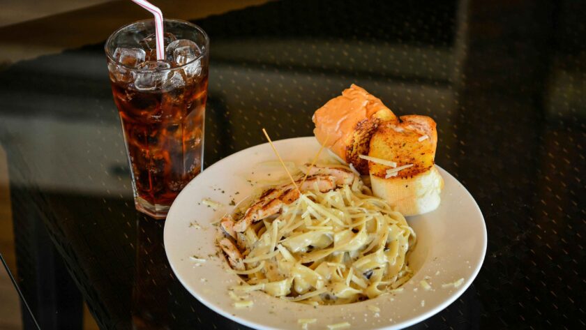 Close-Up Shot of a Plate of Pasta Carbonara beside a Glass of Soft Drink.