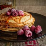 The pancake is served on a black plate and garnished with berries.